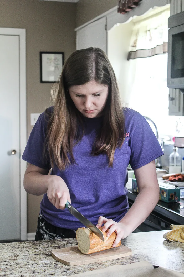 Kayla slicing the loaf of French bread to turn into easy homemade croutons