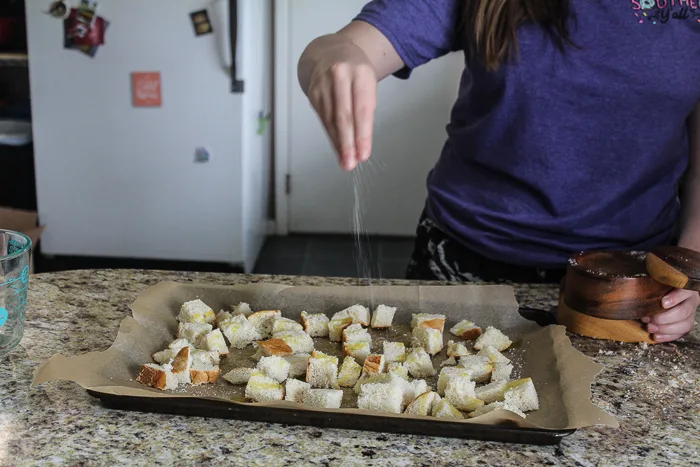 Kayla sprinkling salt on easy homemade croutons