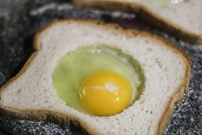 placing egg in the center of the toast for egg in the hole